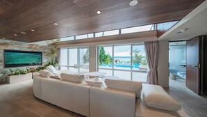 Una sala de estar moderna con un sofá grande, un televisor de pantalla plana y vistas a una piscina y zona exterior.