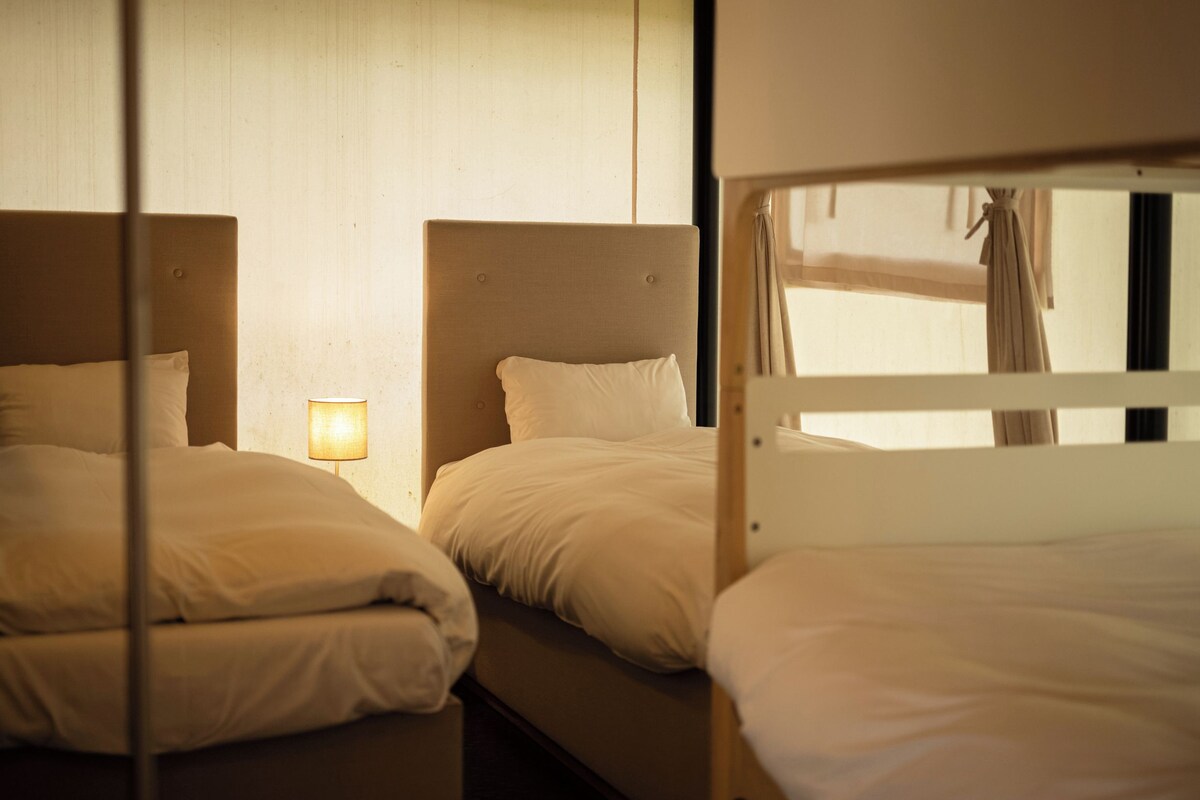 A hotel room with two beds, a bedside lamp, and a window with curtains.
