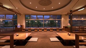 A modern restaurant with a central seating area, large windows offering a view of the outdoors, and a ceiling with recessed lighting. - Stella Glamping Guesthouse (Nakatsugawa)
