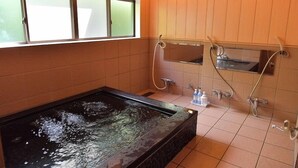 A bathroom with a rectangular hot tub, a mirror, and a shower. - Hotel Cho (Yuzawa)