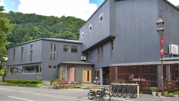 A modern building with a flat roof, large windows, and a small porch area with potted plants. - Hotel Cho (Yuzawa)