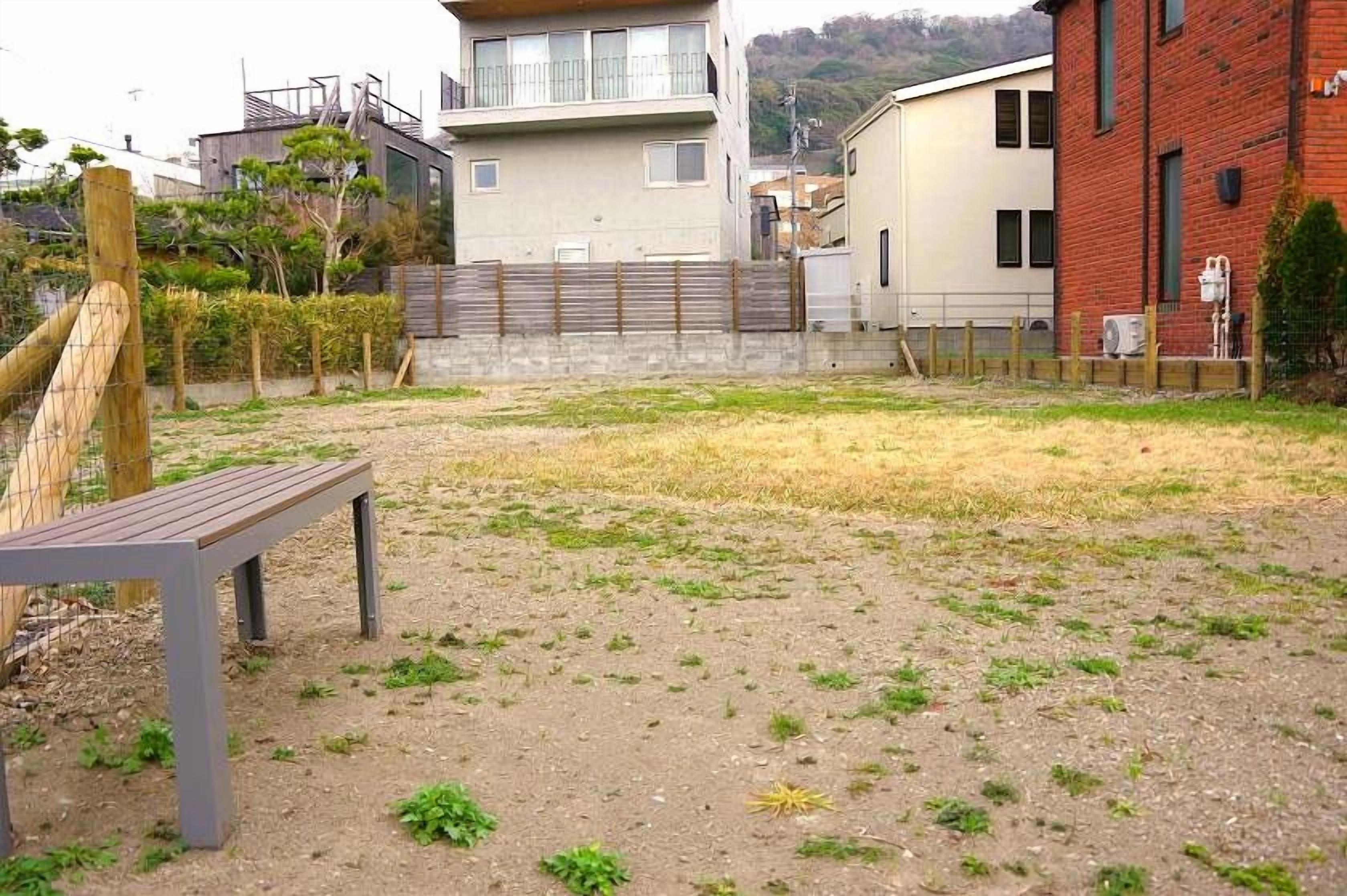 A residential area with a dirt yard, a wooden bench, and modern houses in the background.