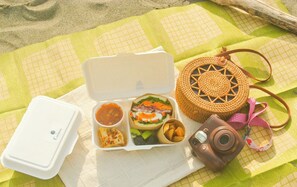 Une table dressée pour un repas, avec un appareil photo et un sac en tissu posés sur une nappe à carreaux.