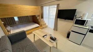 Una camera d'albergo compatta con un letto a castello, un angolo cottura, una televisione a schermo piatto e un divano.