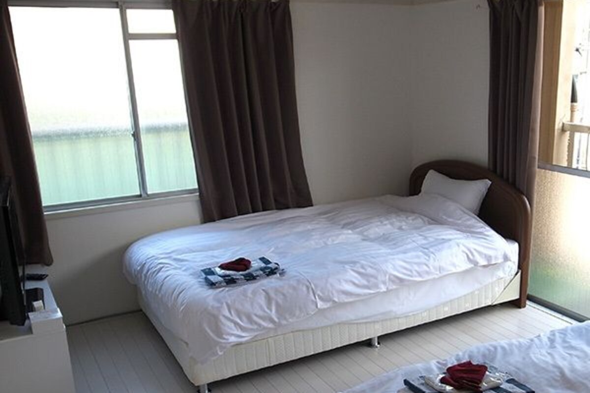 A hotel room with two single beds, a white wardrobe, and a window with curtains.