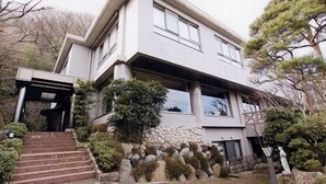 A modern two-story house with a stone facade, a stone staircase, and a well-maintained garden with various shrubs and trees. - Dog's Rest Place (Hakone)