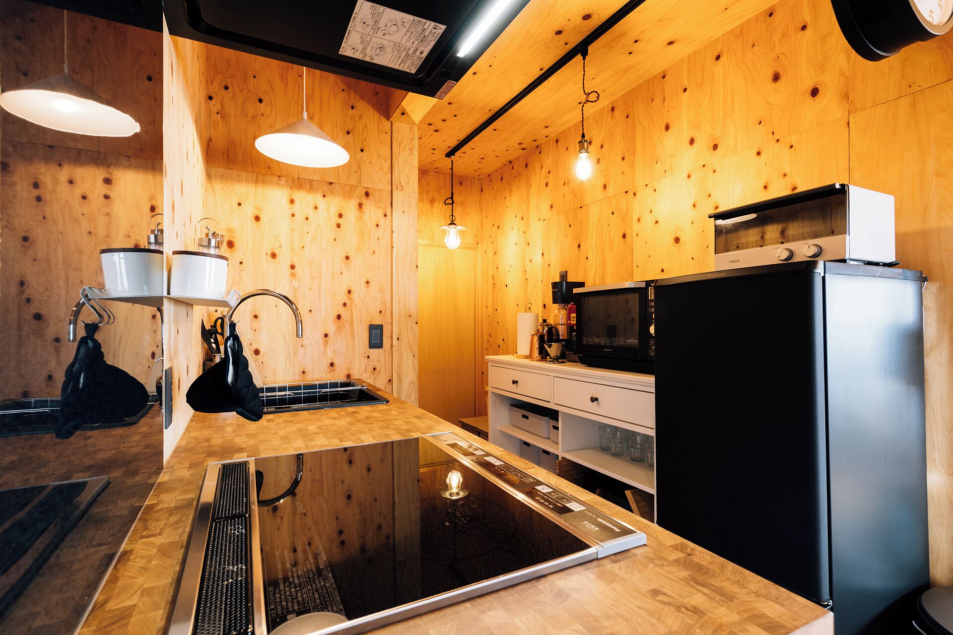 A modern kitchen with wooden walls, a black refrigerator, a microwave, and a stove.