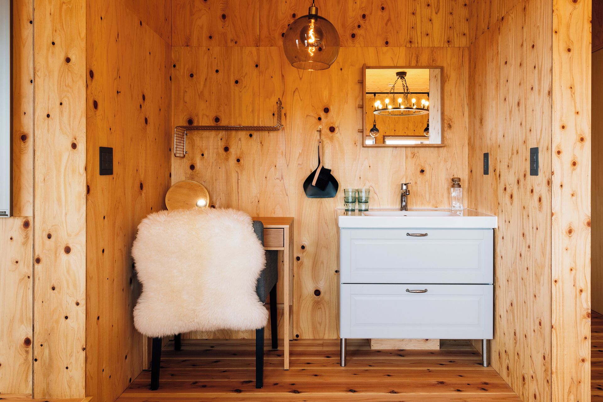 Ein Holzhütten-Interieur mit einem weißen Stuhl, einem weißen Schminktisch mit Spiegel und einer Hängelampe.