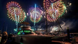 Un barco atracado en un puerto deportivo con fuegos artificiales al fondo.