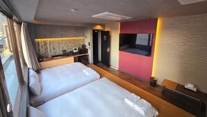 A hotel room with two beds, a small desk, a TV mounted on the wall, and a window with curtains. - Ping Pong Hotel & Cabin Tokuyama Ekimae / Ping Pong Residence Kojimachi (Shunan)