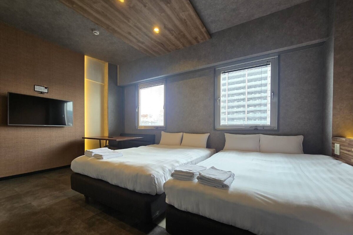 Ein Hotelzimmer mit zwei Betten, einem flachbildfernseher an der Wand und einem Fenster mit Jalousien.
