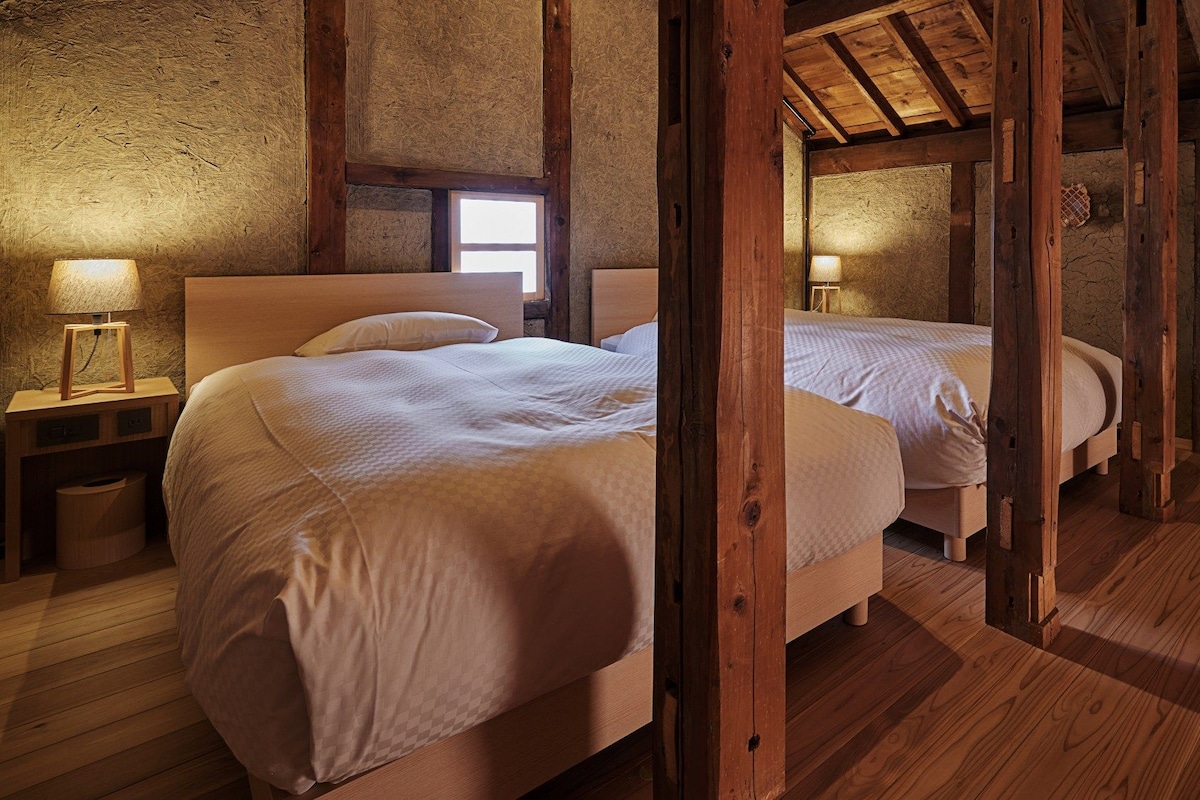 A rustic wooden room with two beds, a nightstand, and a window.