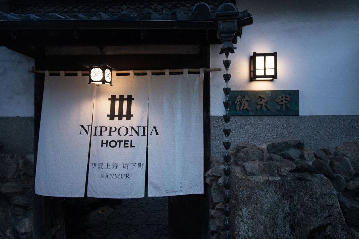 A sign for the Nipponia Hotel with a lantern and stone wall.