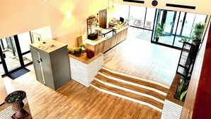 Un espace d’accueil moderne, doté d’un comptoir de réception en bois, d’un coin salon avec des fauteuils et offrant une vue sur l’extérieur grâce à de grandes fenêtres.