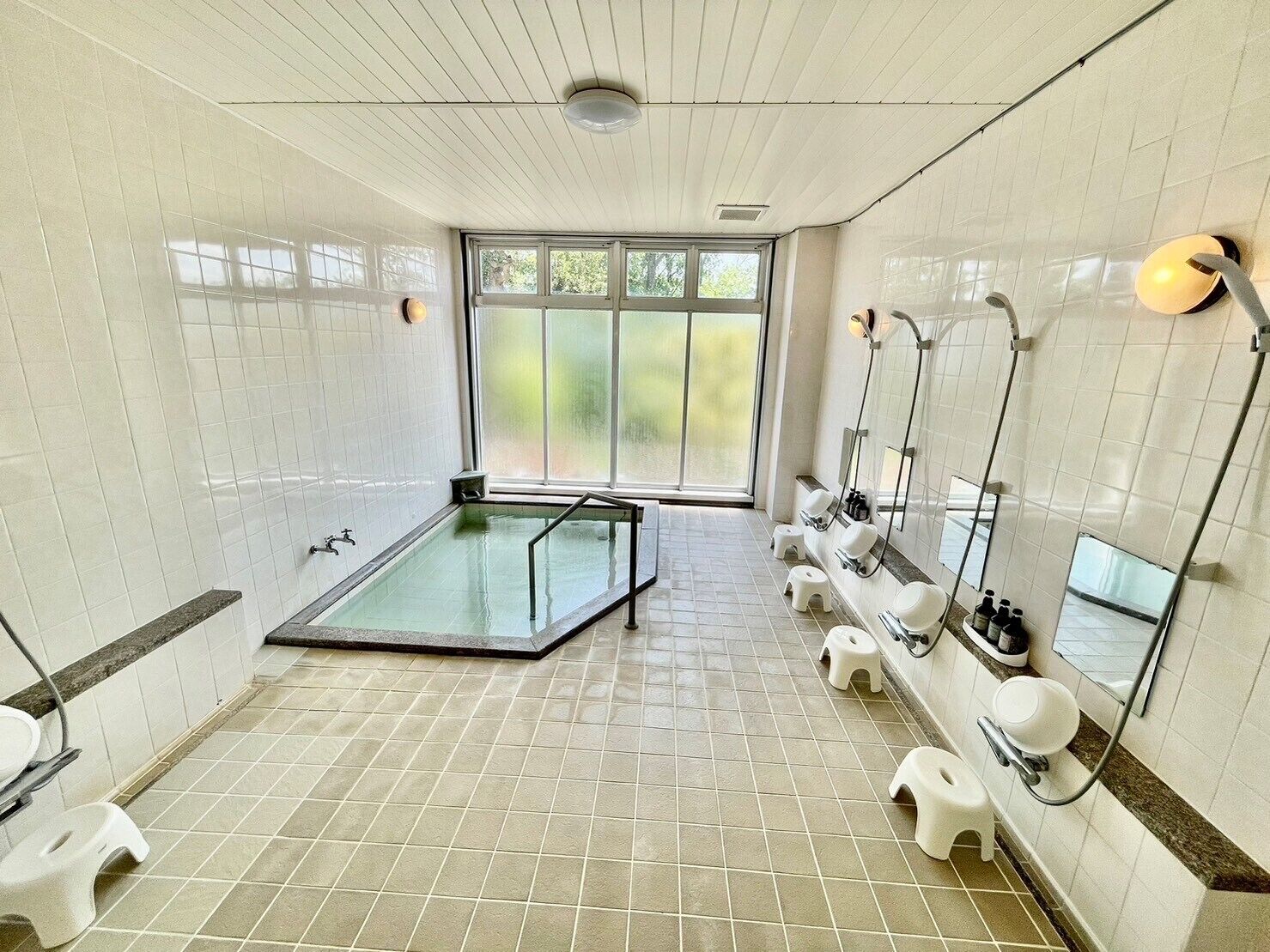 Une salle de bain moderne dotée d’un jacuzzi entouré de parois en verre, de plusieurs lavabos et d’une grande fenêtre laissant entrer la lumière naturelle.