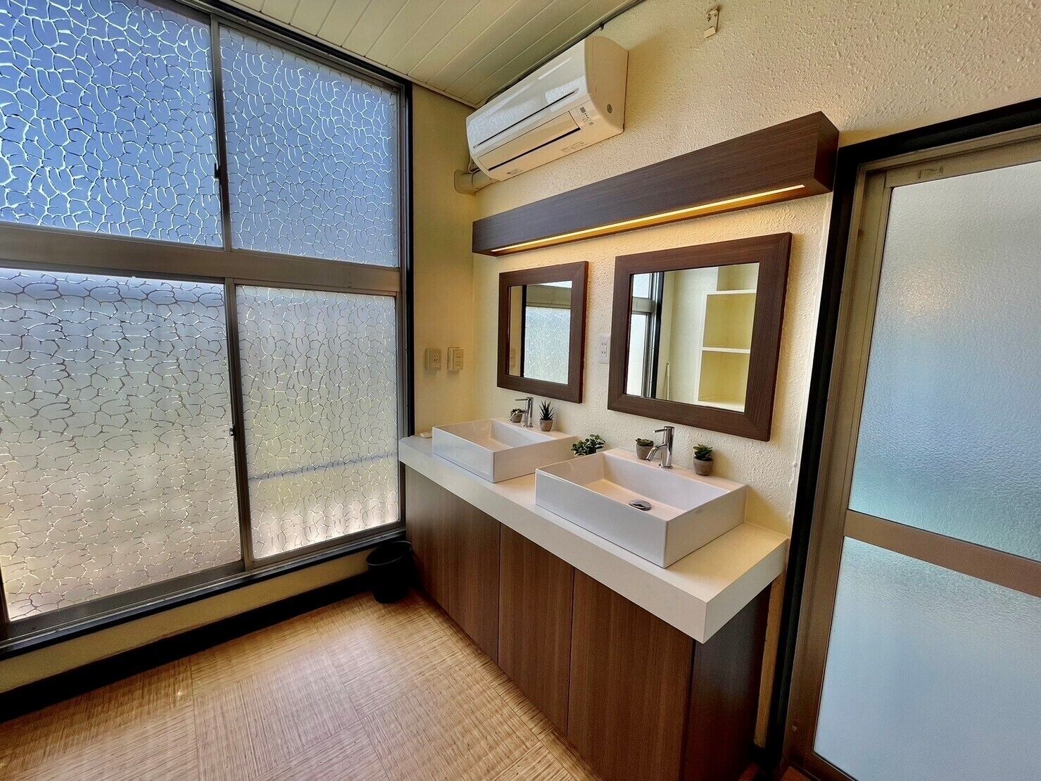 A modern bathroom with two sinks, frosted glass windows, and wooden cabinetry.