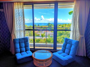 A room with two blue armchairs, a wicker coffee table, and a large window with a view of a balcony and the sea. - Isola Izu Kogen (Ito)