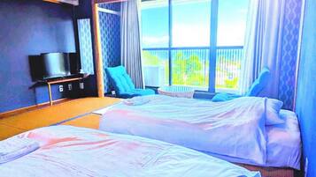 A hotel room with two beds, a TV, a chair, and a balcony with curtains.