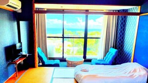 Une chambre d’hôtel avec deux lits, une télévision, une fenêtre donnant sur la mer et une petite table avec une chaise.