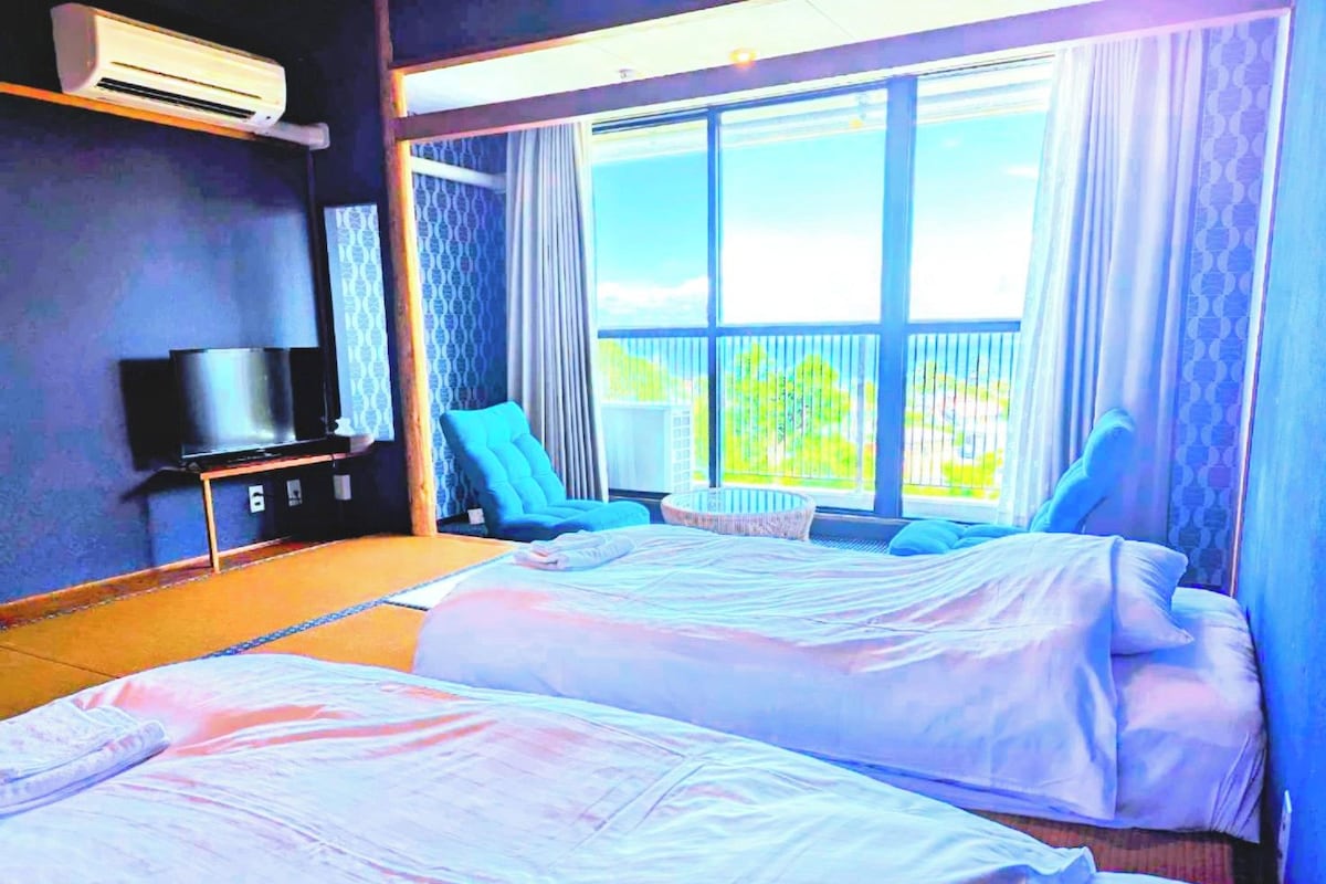 A hotel room with two beds, a TV, a chair, and a balcony with curtains.