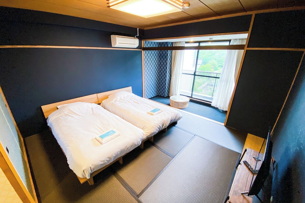 A room with two beds, a window with curtains, a ceiling light, and a small table.