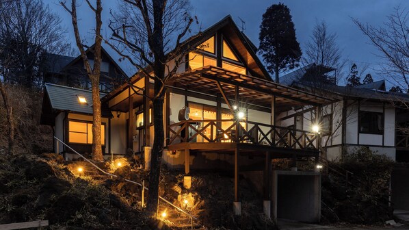 A modern house with a wooden deck, large windows, and a well-lit interior. - Mori no Kiki (Minamioguni)