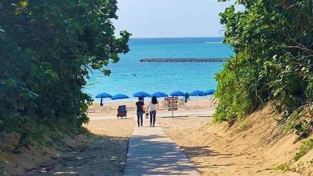 A beach pathway leading to the sea with blue umbrellas and a signboard. - Hotel Fit In Ishigakijima (Ishigaki)