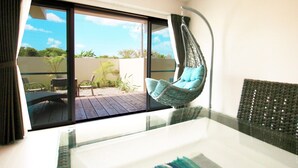 A room with a glass table, a hanging chair with cushions, and a view of an outdoor deck with chairs and plants. - Hotel Fit In Ishigakijima (Ishigaki)