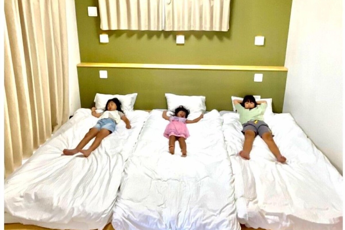 A room with three beds aligned in a row, each with white bedding and a green wall behind.