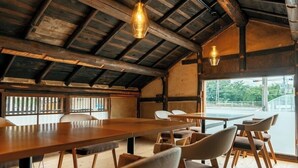 Un intérieur rustique en bois, avec une longue table et des chaises, de grandes fenêtres et des luminaires suspendus.
