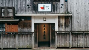 Un bâtiment rustique avec une façade en bois, une enseigne arborant un logo rouge et vert, et une entrée de style japonais traditionnel.