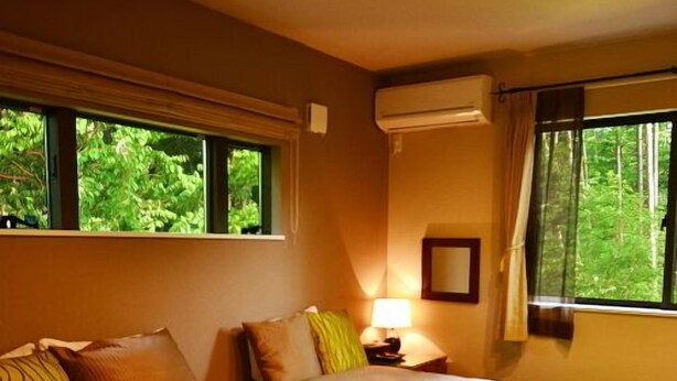 Een hotelkamer met twee bedden, een raam met uitzicht op groen, een airconditioningsapparaat en een nachtkastje met een lamp.