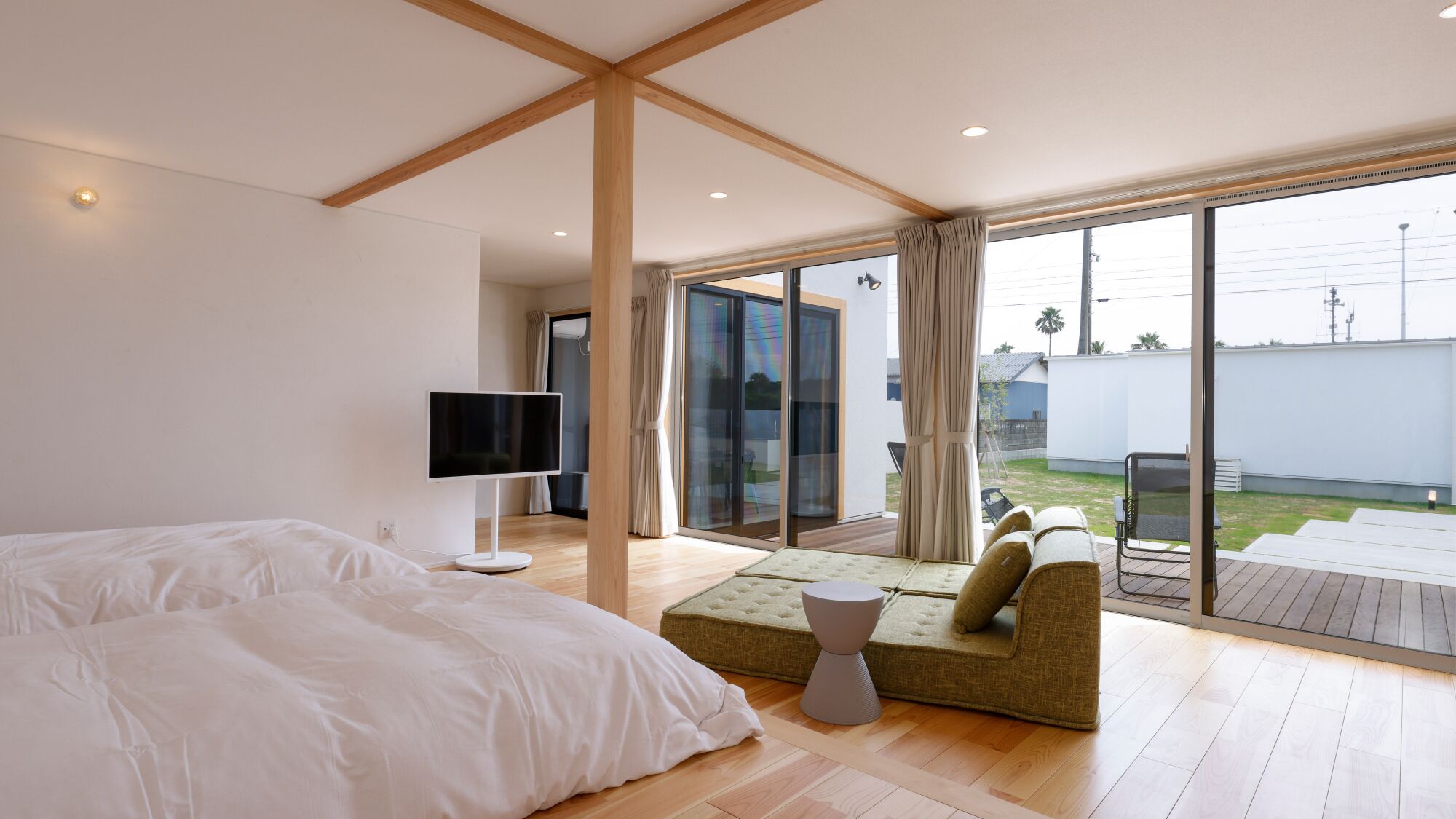 A modern bedroom with a large bed, a TV, and a sofa by a sliding glass door leading to a balcony.