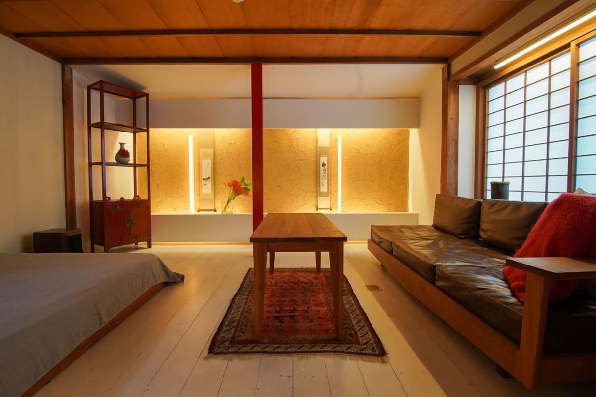 A modern living room with a wooden floor, a sofa, a table, and a bookshelf.