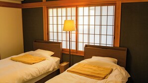 A room with two single beds, a nightstand, a lamp, and a window with a grid pattern. - Otomari Chuzaemon (Shodoshima)