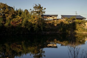 A house with a solar panel roof, surrounded by dense trees and a calm lake. - Secret Break Isumi (Isumi)