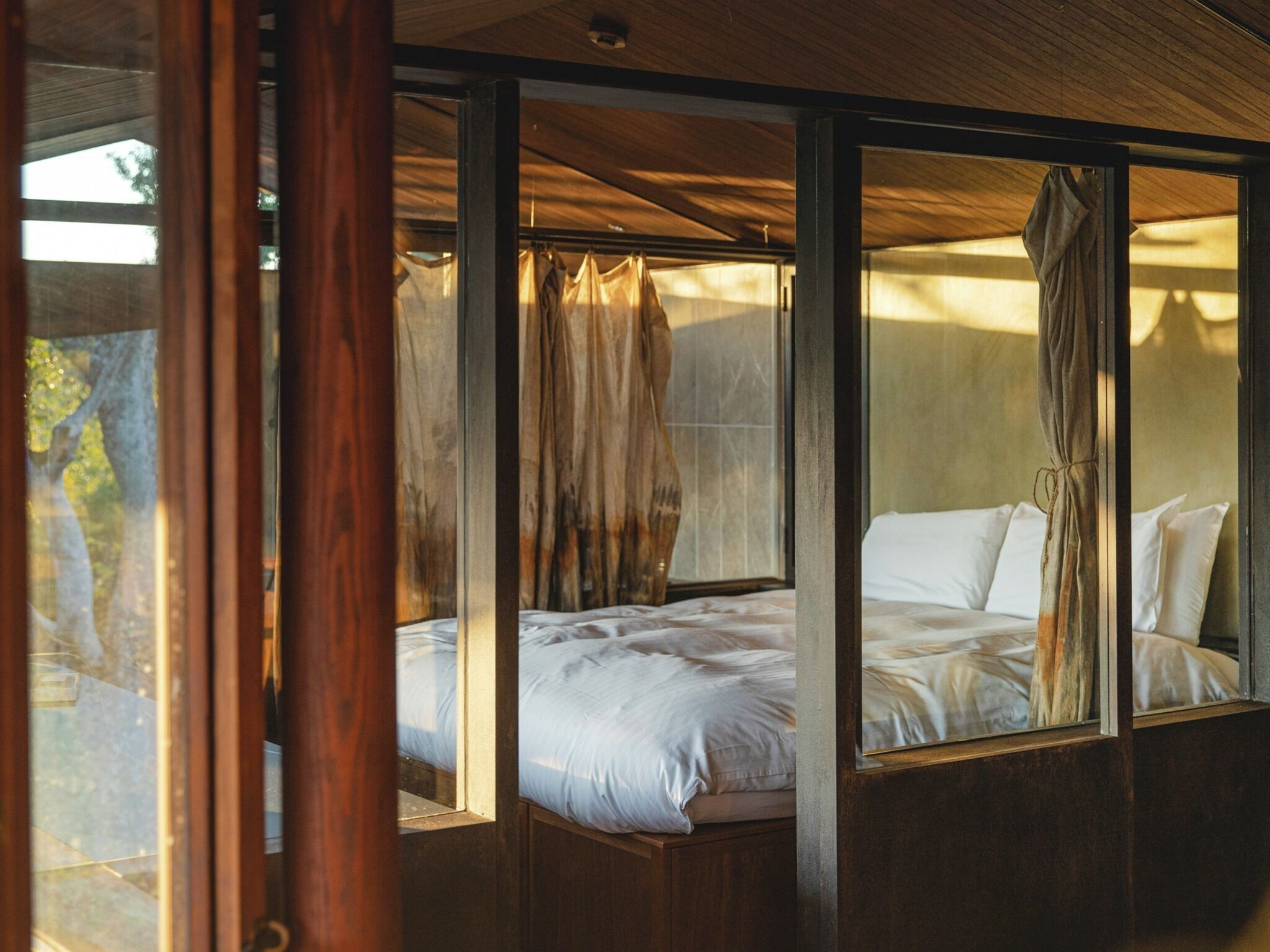 Una habitación con cama, vigas de madera y ventana con cortinas.