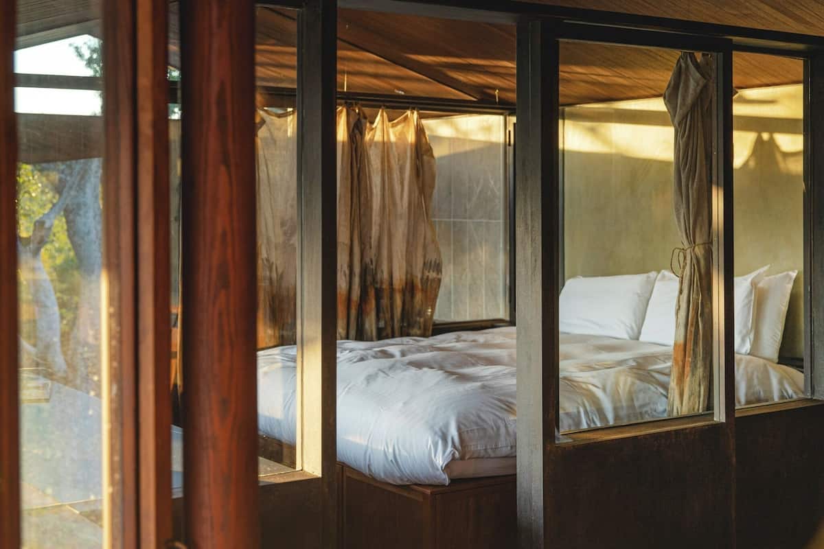 Una habitación con cama, vigas de madera y ventana con cortinas.