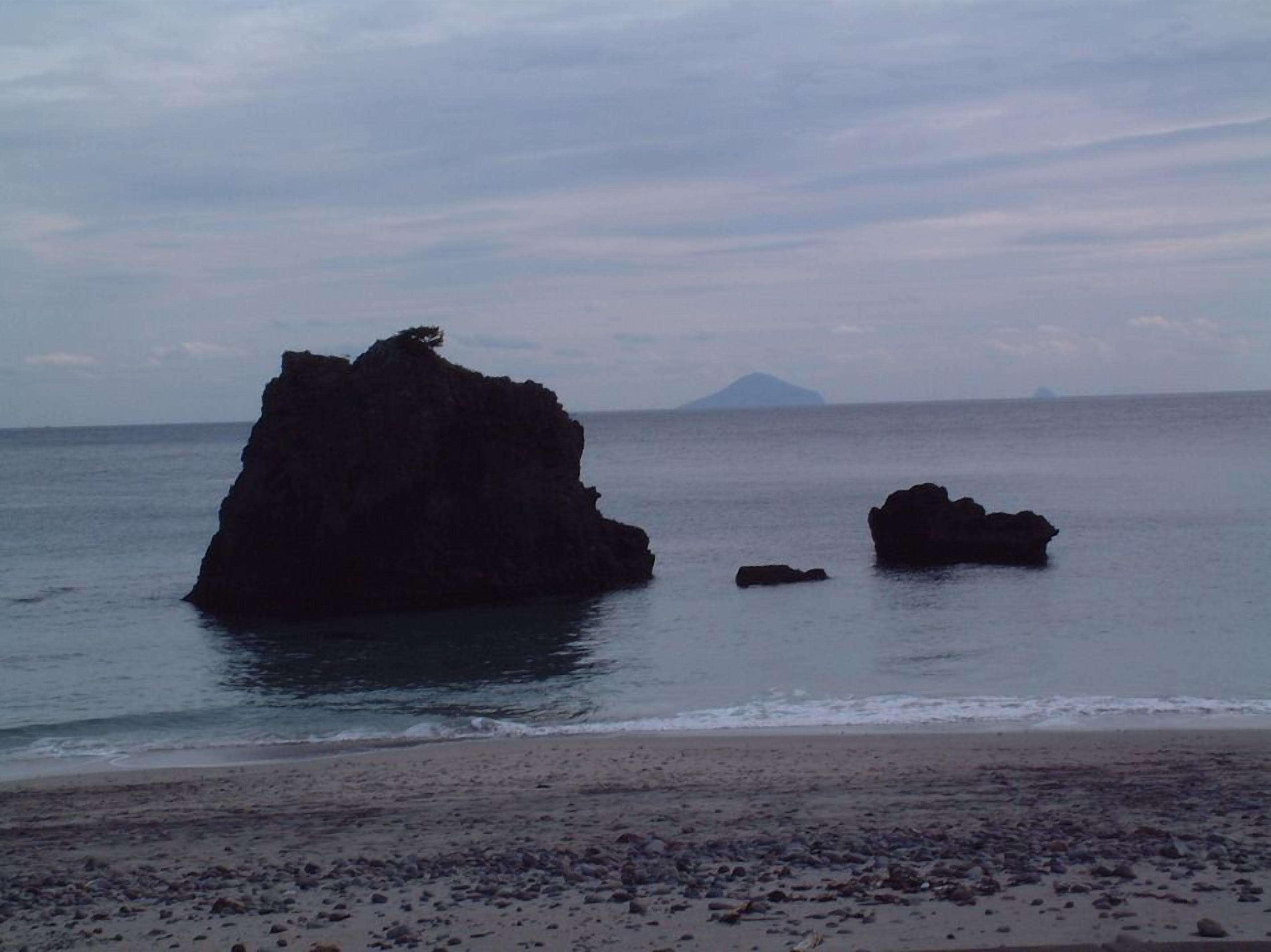 Een strand met grote rotsformaties en een berg in de verte.