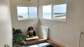 Quarto de canto com duas janelas vista para a praia, um pequeno banco e um radiador.
