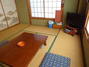 A traditional Japanese room with tatami flooring, a low wooden table, a television on a stand, and a sliding door with a view of the outside. - Izu Shimoda Minshuku Sangenya (Shimoda)