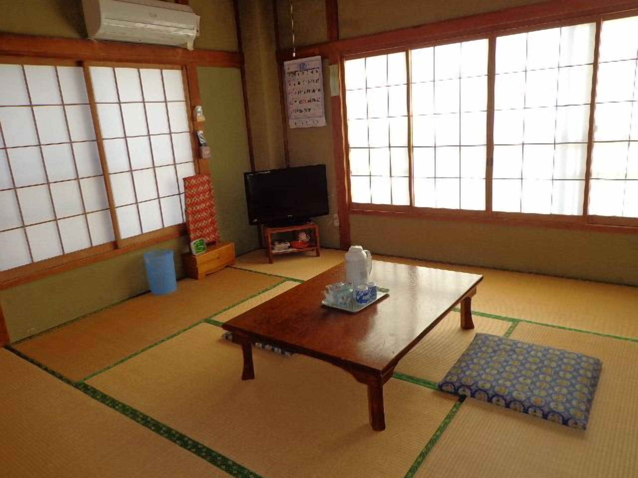 Um quarto japonês tradicional com tatame, uma mesa de madeira baixa, uma televisão e biombos shoji.