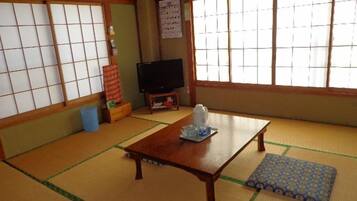 Um quarto japonês tradicional com tatame, uma mesa de madeira baixa, uma televisão e biombos shoji.