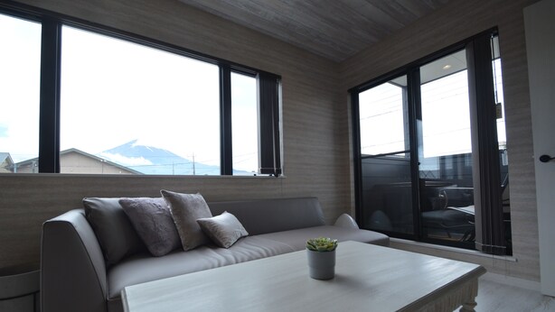 A modern living room with a sofa, a coffee table, and a potted plant. Large windows provide a view of the outside. - Enico. Mt. Fuji Peace (Fujikawaguchiko)