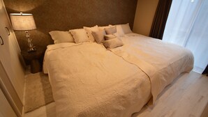 A neatly made bed with a textured blanket and multiple pillows, a bedside lamp, and a wooden nightstand. - Enico. Mt. Fuji Peace (Fujikawaguchiko)