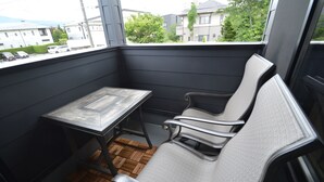 A balcony with a small table and two chairs, wooden flooring, and a view of residential buildings and greenery. - Enico. Mt. Fuji Peace (Fujikawaguchiko)