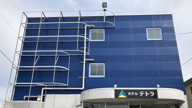 Un edificio con fachada azul, un letrero con caracteres japoneses y una estructura metálica a un lado.