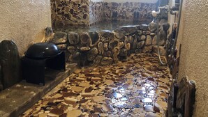 A bathroom with a mosaic floor, stone walls, and a black toilet. - Shoraku Ryokan (Ozu)