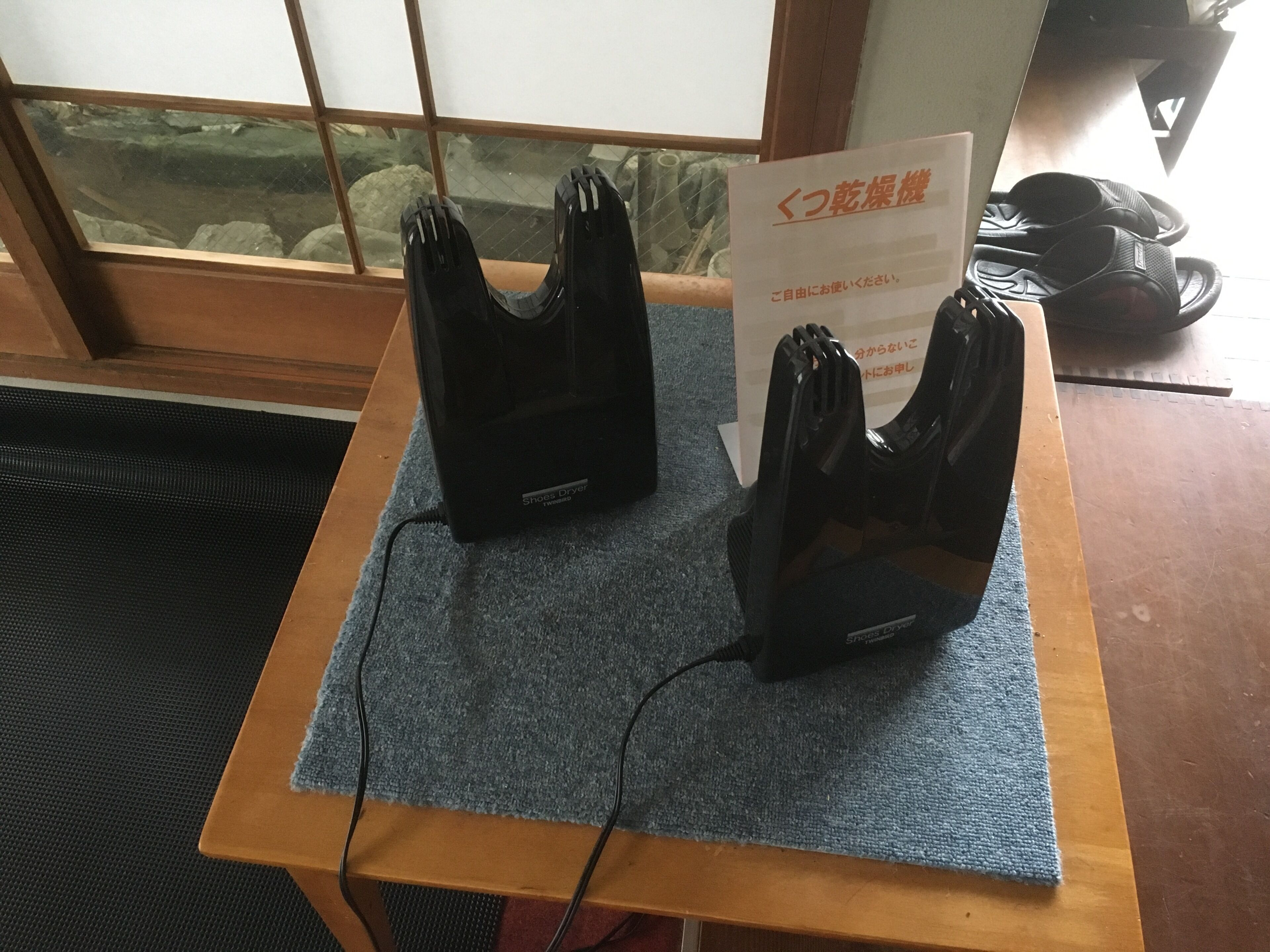 A wooden table with a blue mat, two black shoe dryers, and a sign in Japanese.