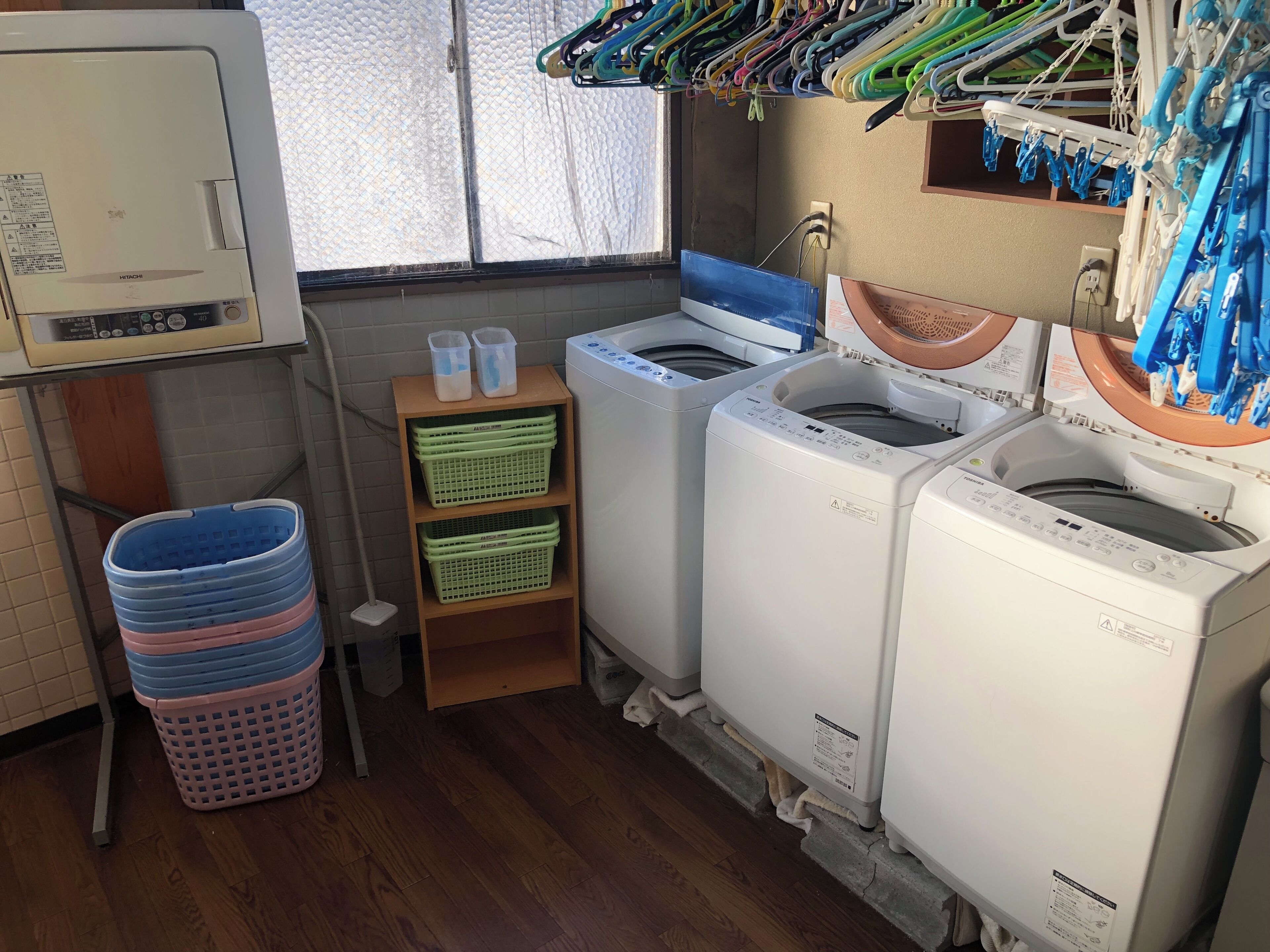 A laundry room with two washing machines, a shelf with baskets, and a window with laundry hanging.